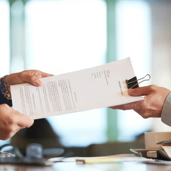 Deux personnes échangent des documents à une table, engagées dans une discussion ou une collaboration.