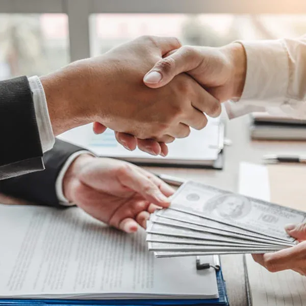 Two business professionals shaking hands over a stack of cash, symbolizing a successful deal or agreement.
