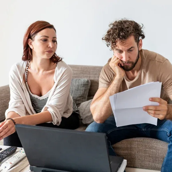 Un couple consulte des documents sur un ordinateur portable, assis côte à côte sur un canapé.