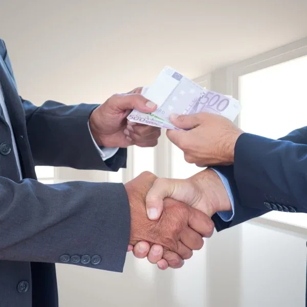 Two businessmen shaking hands, symbolizing a successful deal, with stacks of money visible in the background.