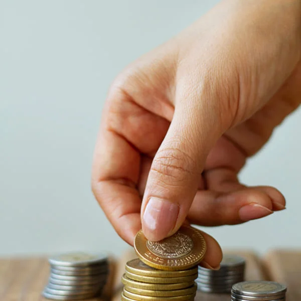 A person placing coins on a wooden table, focusing on the arrangement of the coins.