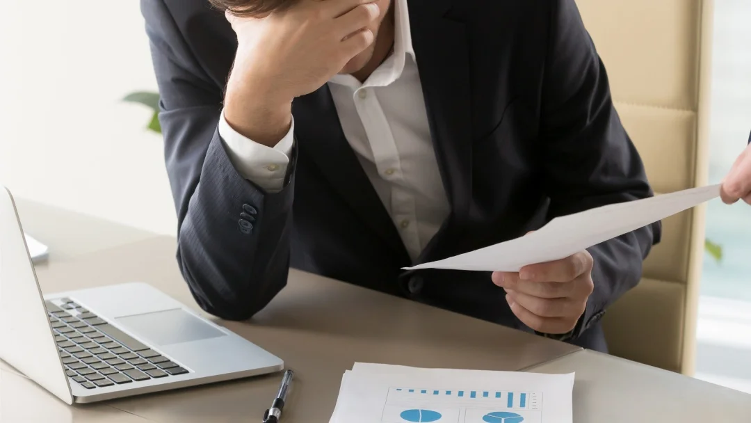 A man in a suit examines a document, appearing focused and engaged in his work.