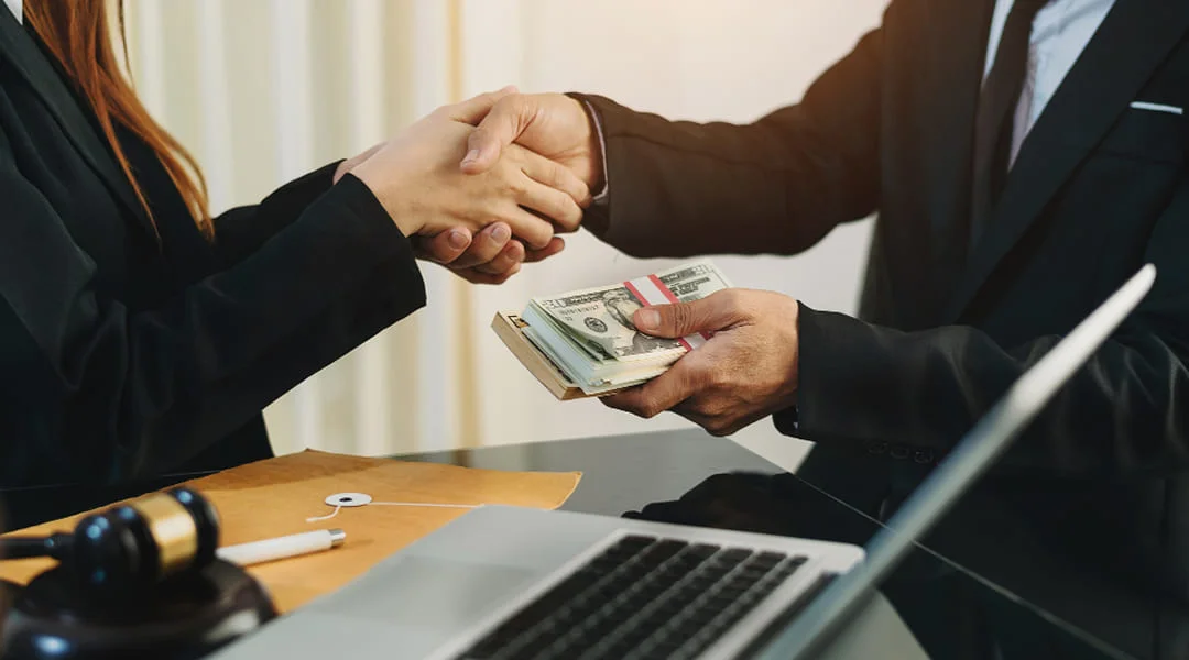 A man and woman shaking hands over a stack of cash, symbolizing a business agreement or financial transaction.