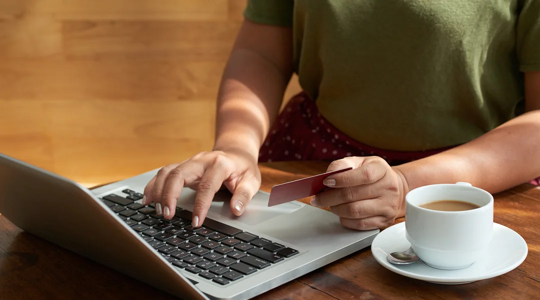 A person typing on a laptop while holding a credit card, likely making an online purchase.
