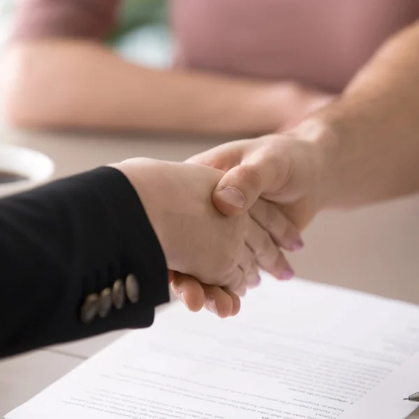 Deux personnes se serrent la main au-dessus d'un document, symbolisant un accord ou un partenariat.