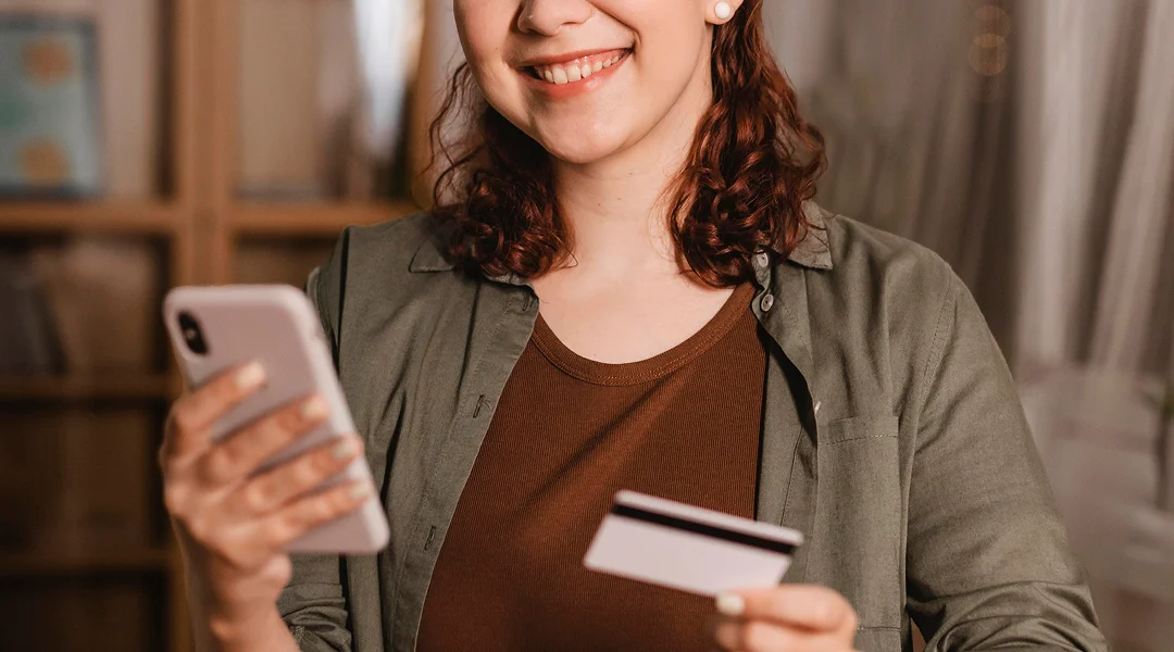 Une femme souriante tenant une carte de crédit.