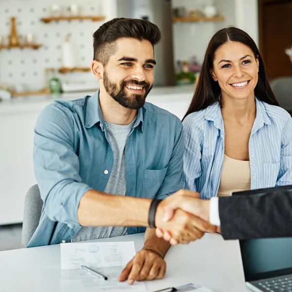 A man and woman shaking hands across a desk, symbolizing agreement or partnership in a professional setting.