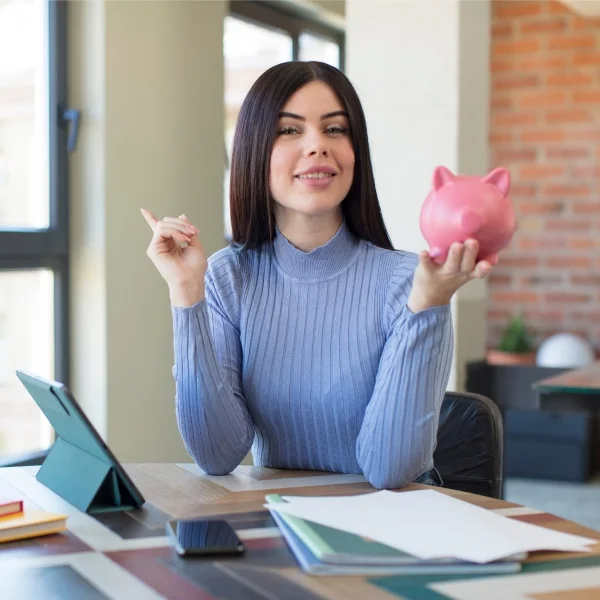 A woman holding a piggy bank in front of her laptop, symbolizing saving and financial management.