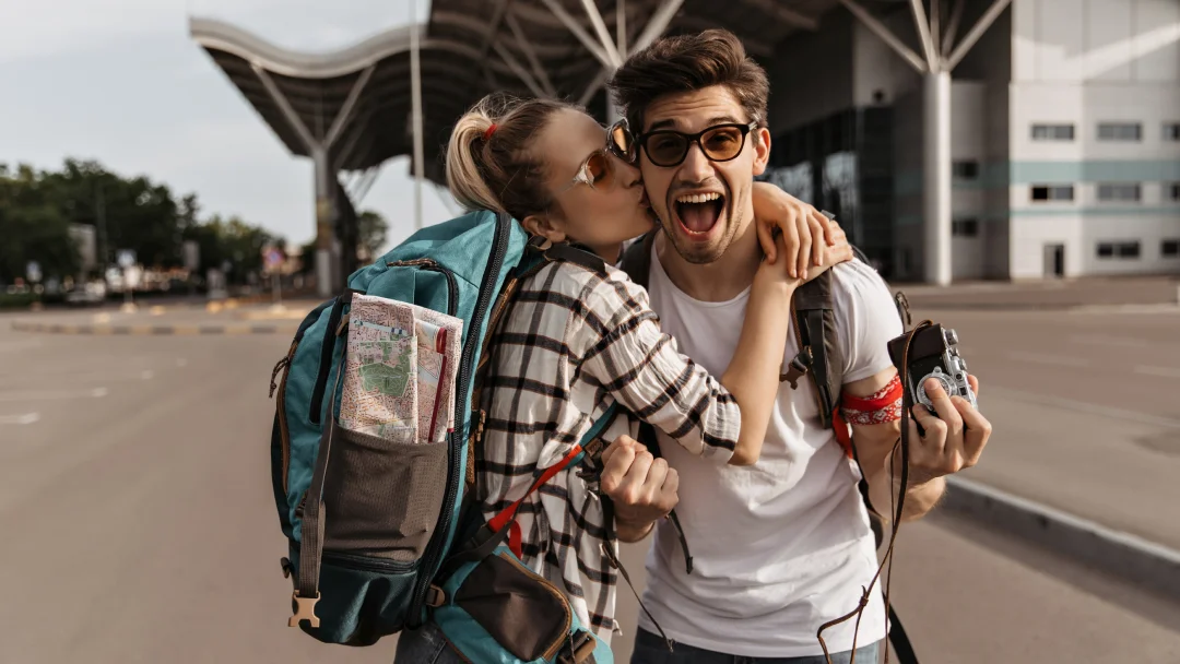 Un homme et une femme s'embrassent en tenant un sac à dos, symbolisant un moment de voyage ensemble.
