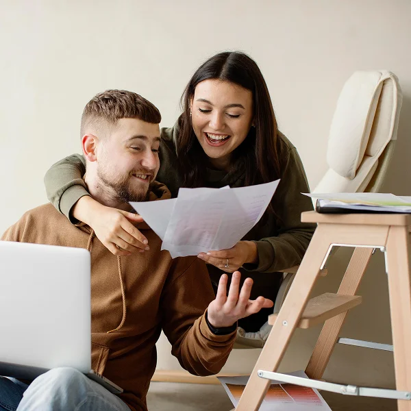 A man and woman sitting on a chair, using a laptop to discuss a $500 and up loan.